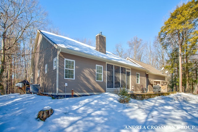 snow covered rear of property featuring central air condition unit and a chimney