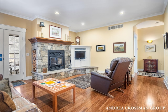 living room featuring arched walkways, a stone fireplace, wood finished floors, visible vents, and ornamental molding