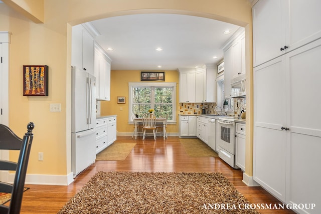 kitchen featuring arched walkways, light countertops, white appliances, and white cabinets