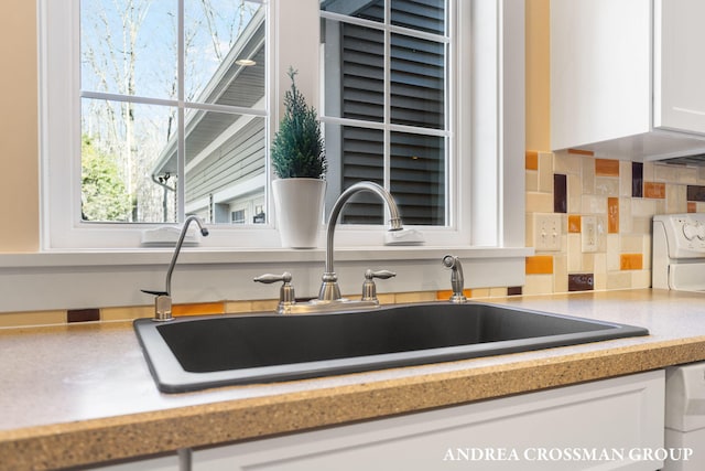 kitchen featuring dishwashing machine, a sink, white cabinetry, light countertops, and decorative backsplash