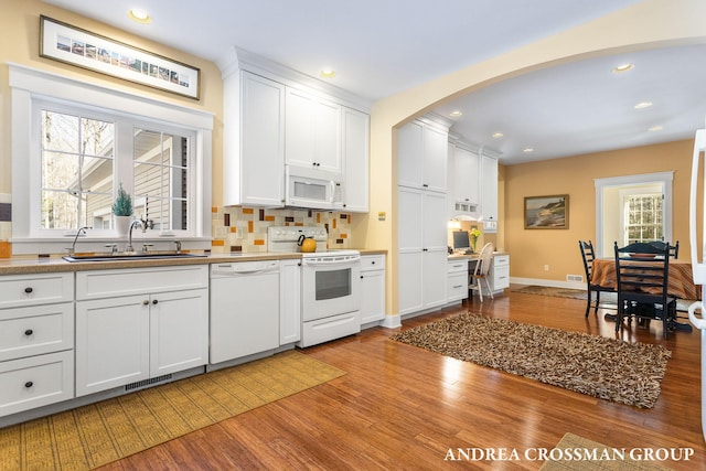 kitchen with arched walkways, white appliances, a sink, white cabinetry, and light wood-type flooring