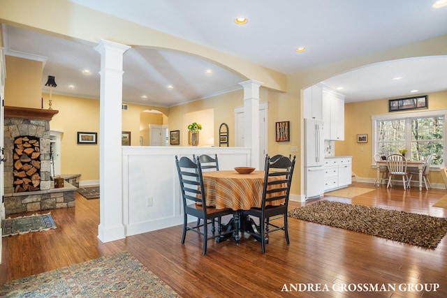 dining space featuring decorative columns, a stone fireplace, baseboards, and wood finished floors