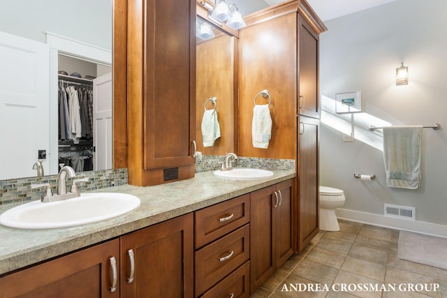 full bathroom featuring double vanity, decorative backsplash, a walk in closet, and a sink