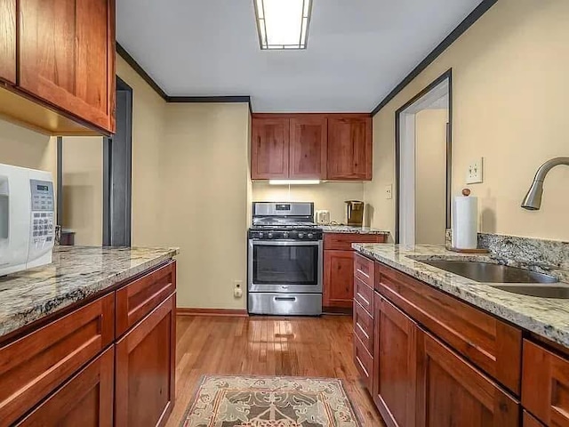 kitchen with light stone counters, a sink, stainless steel gas range oven, and ornamental molding