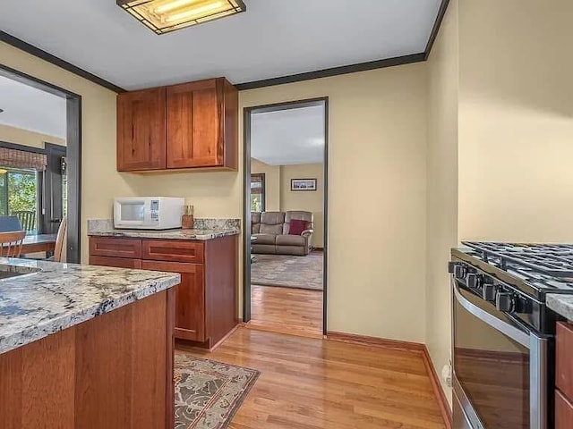 kitchen with white microwave, light wood-style flooring, gas range, light stone countertops, and crown molding