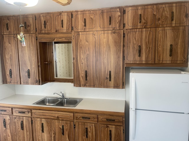 kitchen featuring light countertops, brown cabinetry, a sink, and freestanding refrigerator