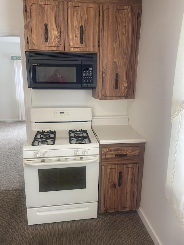 kitchen with white gas range oven, brown cabinets, light countertops, dark colored carpet, and black microwave