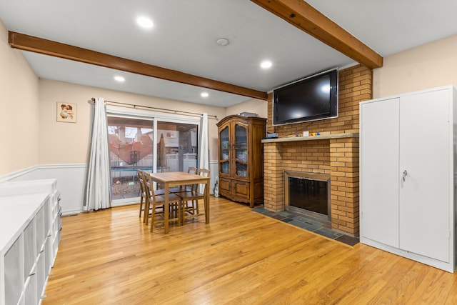 dining room featuring light wood-style floors, recessed lighting, a brick fireplace, and beamed ceiling