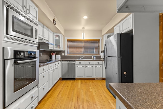 kitchen with dark countertops, appliances with stainless steel finishes, glass insert cabinets, white cabinetry, and under cabinet range hood