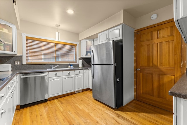 kitchen with stainless steel appliances, dark countertops, light wood-style floors, glass insert cabinets, and a sink