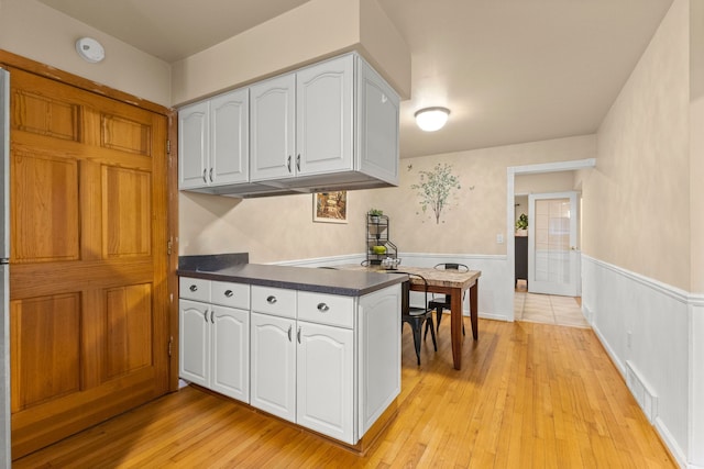 kitchen featuring visible vents, wainscoting, dark countertops, light wood-style flooring, and white cabinetry