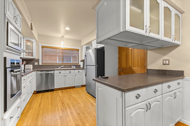 kitchen with light wood-style flooring, stainless steel appliances, white cabinets, dark countertops, and glass insert cabinets