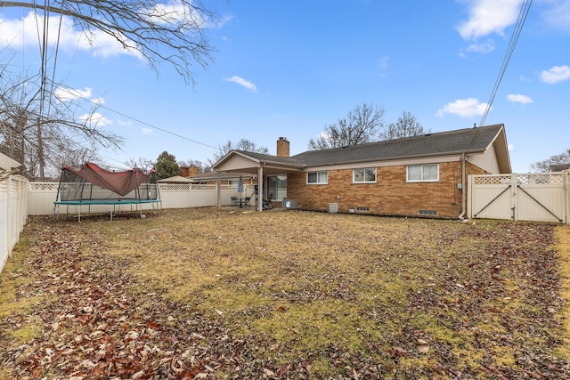 back of house with a fenced backyard, a trampoline, a gate, and brick siding