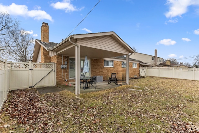 rear view of property with brick siding, a chimney, a gate, a patio area, and a fenced backyard