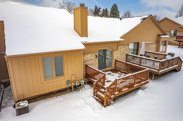 snow covered rear of property featuring a chimney and brick siding