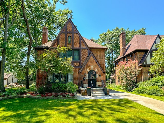 tudor-style house featuring brick siding, a chimney, and a front lawn