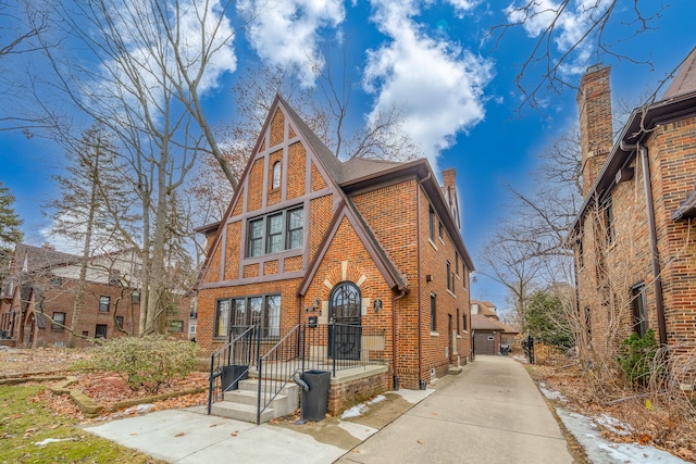 english style home featuring a chimney, an outbuilding, a detached garage, and brick siding