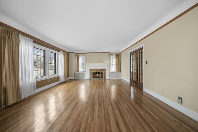 unfurnished living room with ornamental molding, a fireplace, baseboards, and wood finished floors