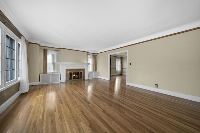 unfurnished living room with baseboards, radiator, wood finished floors, crown molding, and a fireplace