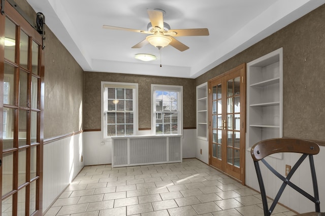 interior space with a ceiling fan, french doors, and a wainscoted wall