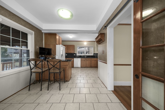 kitchen with a peninsula, white appliances, a breakfast bar, brown cabinetry, and dark countertops