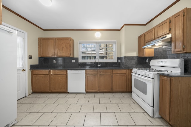 kitchen featuring under cabinet range hood, white appliances, a sink, ornamental molding, and dark countertops