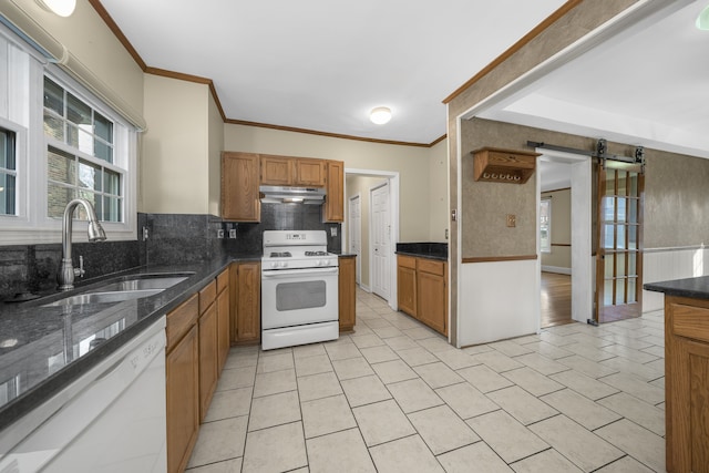 kitchen with a barn door, under cabinet range hood, white appliances, a sink, and decorative backsplash