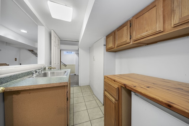 kitchen with light tile patterned floors, wood counters, brown cabinetry, and a sink