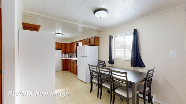 kitchen with light countertops, freestanding refrigerator, light floors, brown cabinetry, and crown molding