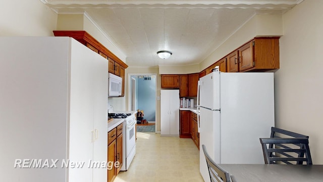 kitchen with light floors, light countertops, brown cabinetry, ornamental molding, and white appliances