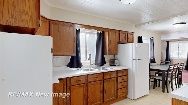 kitchen with light countertops, a sink, freestanding refrigerator, and brown cabinets