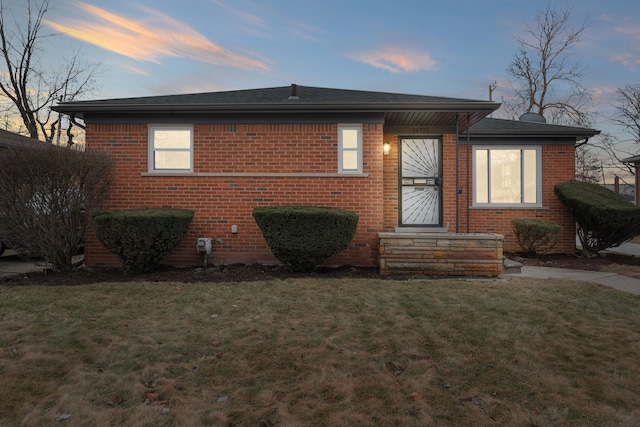 bungalow-style home featuring roof with shingles, brick siding, and a lawn