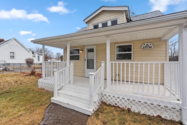 view of front of home with a porch, roof with shingles, a front lawn, and fence