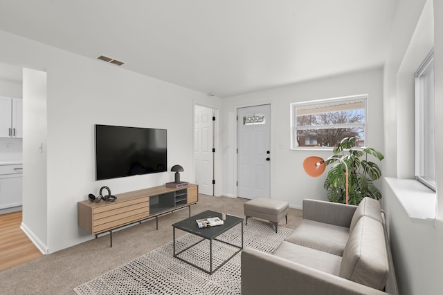 living area featuring baseboards, visible vents, and light colored carpet