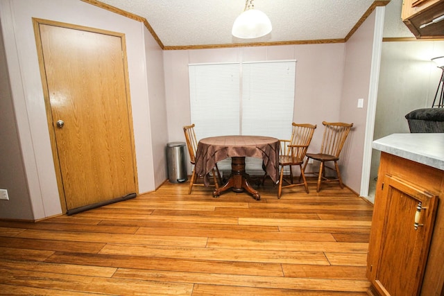 dining area with light wood-style flooring, a textured ceiling, and crown molding