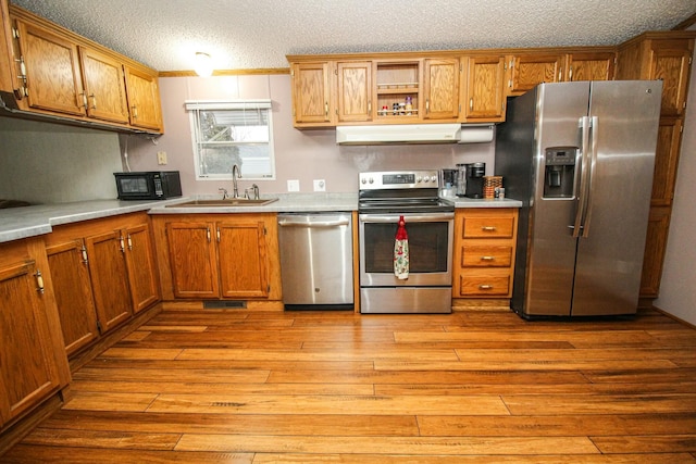 kitchen featuring under cabinet range hood, stainless steel appliances, a sink, light countertops, and brown cabinetry