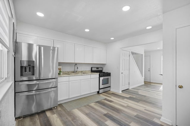 kitchen featuring stainless steel appliances, a sink, light wood-style flooring, and white cabinets