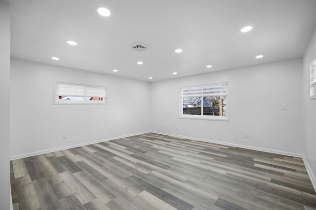 empty room with a wealth of natural light, wood finished floors, visible vents, and recessed lighting