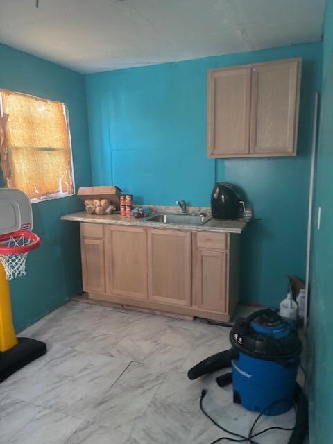 kitchen with marble finish floor, light brown cabinets, light countertops, and a sink