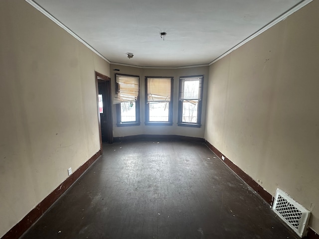 spare room featuring dark wood-style floors, ornamental molding, visible vents, and baseboards