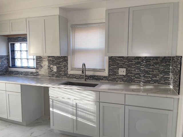 kitchen featuring marble finish floor, a sink, white cabinetry, and decorative backsplash