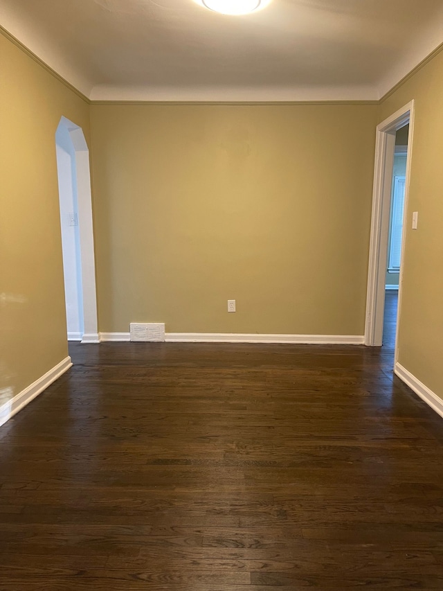 unfurnished room featuring visible vents, arched walkways, dark wood finished floors, baseboards, and crown molding