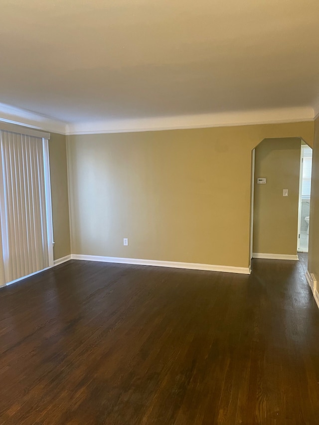 spare room featuring dark wood-style floors, arched walkways, and baseboards