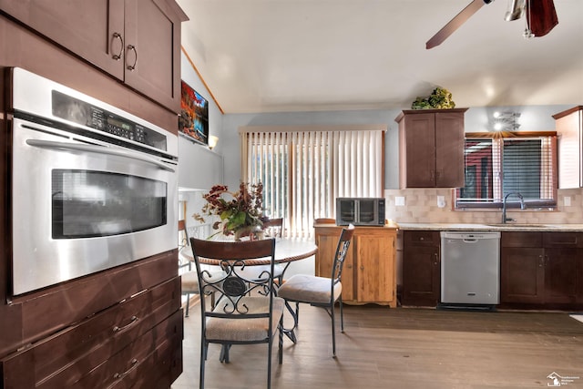 kitchen with a sink, a ceiling fan, appliances with stainless steel finishes, light wood finished floors, and tasteful backsplash