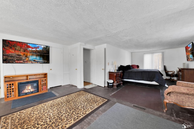 bedroom featuring a glass covered fireplace, finished concrete flooring, and a textured ceiling