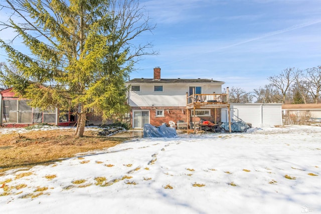 snow covered house featuring a chimney, fence, and brick siding