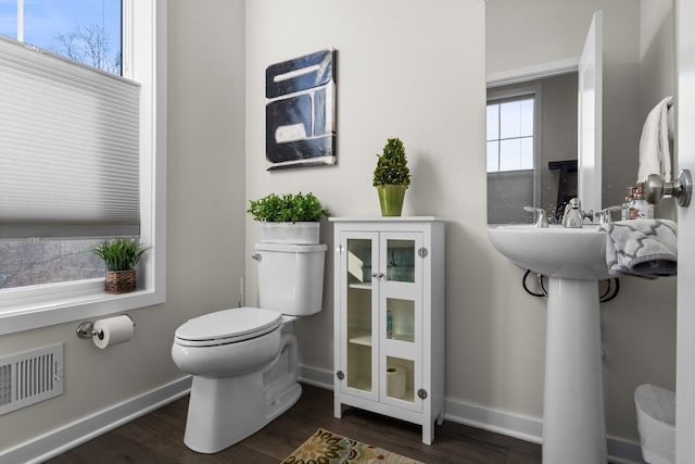 half bath with toilet, visible vents, baseboards, and wood finished floors