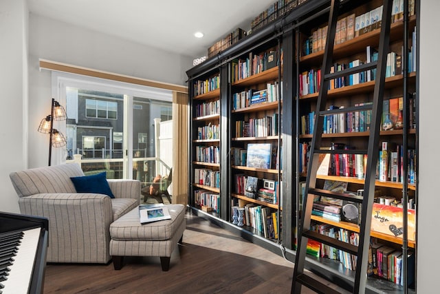 living area with recessed lighting, wall of books, and wood finished floors