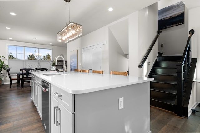 kitchen featuring dark wood-style flooring, a kitchen island with sink, light countertops, white cabinetry, and a sink