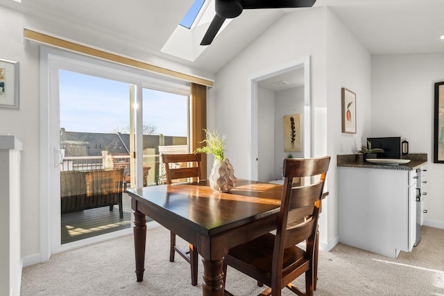 dining space with vaulted ceiling with skylight and light colored carpet